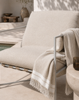 Beige lounge chair with a blanket draped over it in an outdoor setting.