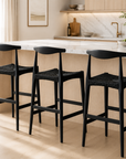 Black bar stools in a modern kitchen with marble countertop and wooden cabinets.