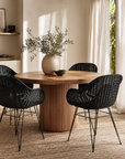 Dining room with a wooden table and black chairs, featuring a vase with greenery.