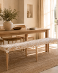 Dining room with wooden table and bench, natural light streaming in.