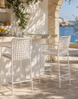 Outdoor setting with a table and two chairs near a stone wall and ocean view.