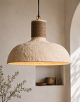 Textured pendant light with rope detail hanging in a room with shelves and plants.