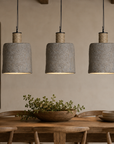 Three gray pendant lights hanging above a wooden dining table with plants and decor.