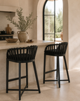 Two black bar stools in a kitchen setting with a window and decorative elements.