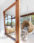 Natural wicker hanging chair with a thick white cushion, showcasing a coastal-inspired design perfect for indoor and outdoor settings