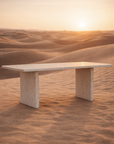 Amani dining table in dune finish with rectangular tabletop and sculptural pedestal legs set in a warm desert landscape