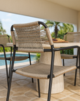Close-up of outdoor rope weave dining chair with black metal frame styled around a stone dining table beside a pool in a tropical setting.