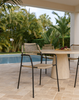 Outdoor dining chair with natural rope weave and black metal frame styled by a poolside stone table in a tropical garden setting.