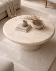 Ayanda coffee table in dune hydro dipped finish with round top and sculptural pedestal base styled in a soft neutral living room.