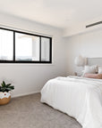 A serene bedroom featuring a neutral-toned upholstered bed with soft layered bedding, a natural rattan armchair with textured cushions, and delicate pendant lighting for a calming retreat.