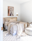 Tranquil bedroom featuring a bedhead in natural linen, styled with layered bedding and a round occasional chair in a soft, light-filled setting