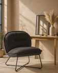Black upholstered occasional chair with sleek metal legs, styled in a neutral-toned room with a timber desk, pampas grass vase, and soft natural light.