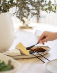 A stylish black mini cheese cutlery set from KULALA Living, featuring a fork, knife, and spreader elegantly arranged on a ceramic platter with brie cheese and crackers, creating a sophisticated and inviting dining scene