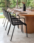Close-up of black rope outdoor dining chairs paired with an oval timber dining table, styled with neutral napkins, ceramic plates, and wine glasses in a lush garden setting.