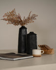 Minimalist decor featuring black wooden vases, a ceramic cup on a wooden coaster, and a neutral-toned tabletop setting for a refined aesthetic
