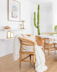 A beautifully styled natural rattan armchair with a white cushion, draped with a textured throw and paired with soft neutral décor, creating a warm and inviting boho-inspired interior.