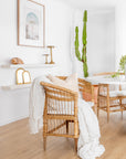 A beautifully styled natural rattan armchair with a white cushion, draped with a textured throw and paired with soft neutral décor, creating a warm and inviting boho-inspired interior.