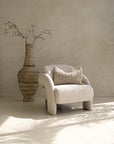 Ivory boucle armchair with rounded, sculptural design, styled with a textured cushion and oversized ceramic vase, creating a serene modern lounge atmosphere.