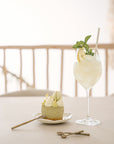 A beautifully styled dessert scene featuring KULALA Living brass dessert spoons, a matcha cheesecake, and a refreshing citrus cocktail. The elegant setting exudes a warm, inviting atmosphere perfect for slow living and indulgence