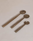 A set of three handcrafted brass spoons from KULALA Living, featuring an artisanal hammered finish and elegantly tapered handles, perfect for serving and stirring with style
