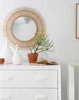 Serene nursery featuring a white dresser and cot, complemented by woven textures, a jute rug, rattan basket, natural decor accents, and a soft linen throw for a warm, organic aesthetic