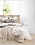 Tranquil coastal bedroom featuring a timber bedhead, layered neutral-toned bedding, woven cushions, and a soft jute rug, styled with white cement vases and a natural fibre laundry basket