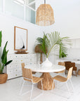 Bright and airy coastal dining space featuring a Kulala Living white ceramic vase with lush greenery, a round wooden dining table, rattan pendant light, and natural wood and metal chairs