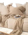 Neutral-toned lounge with oversized cushions, knitted throw and ceramic coffee cup on stacked books creating a cosy, relaxed setting