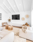 Contemporary white lounge room with high vaulted ceiling, modern upholstered armchairs, rustic wooden coffee tables, woven baskets, and neutral-toned decor