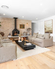 A stylish living space featuring natural linen sofas, a bold black timber coffee table, and a rustic brick fireplace. The neutral palette is complemented by organic décor, textured ceramics, and soft lighting, creating a cosy and sophisticated ambiance