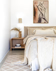 Neutral-toned bedroom featuring the Flynn Open Bedside Table in natural oak, styled with sculptural decor, layered linen bedding, and a textured rug beneath a contemporary artwork