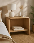Flynn Open Bedside Table in natural oak finish with soft rounded edges, styled with ceramic decor and books in a warm, minimalist bedroom.