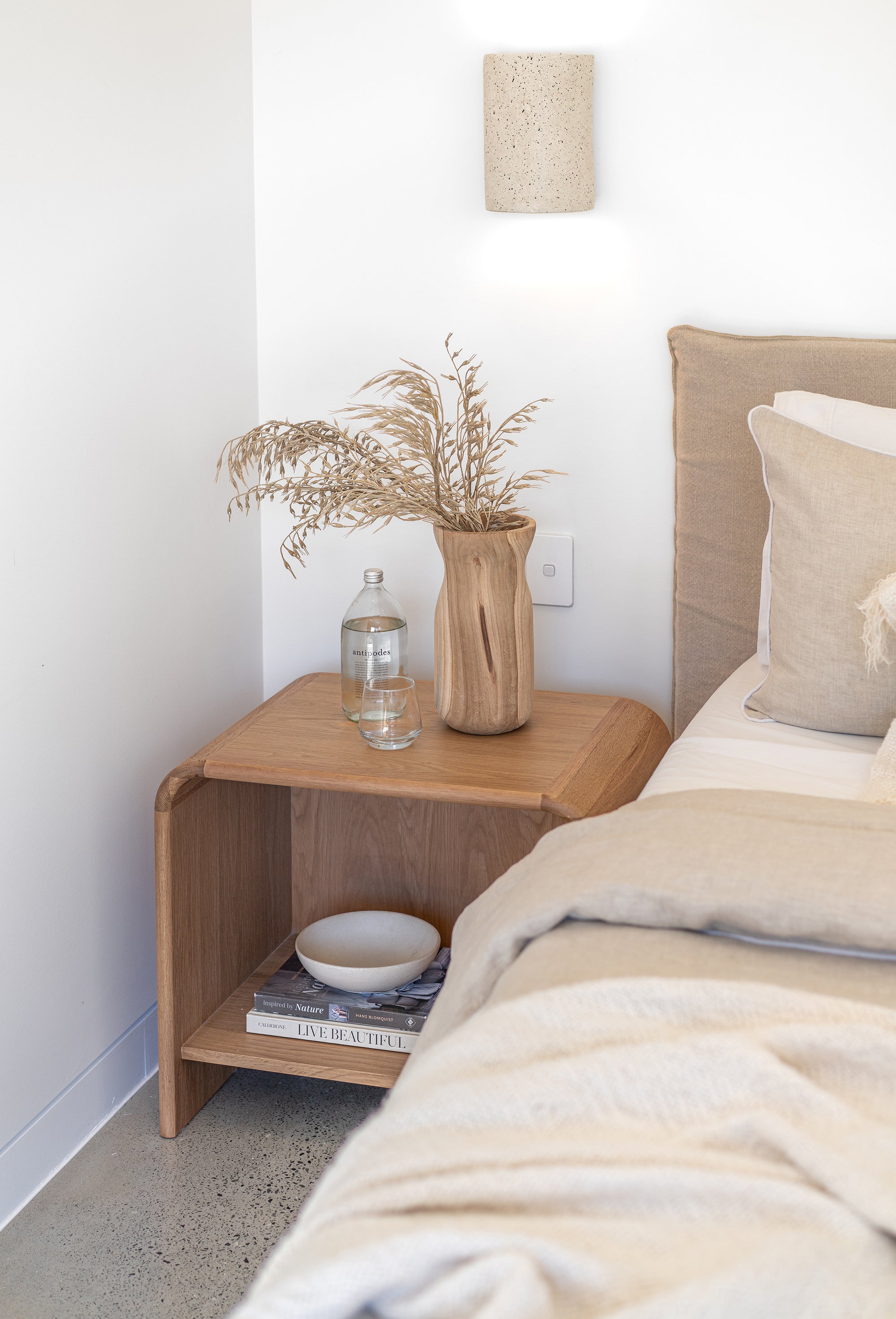 Flynn Open Bedside Table in natural oak styled with a sculptural vase, bedside water, and neutral bedding in a serene contemporary bedroom