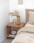 Flynn Open Bedside Table in natural oak styled with a sculptural vase, bedside water, and neutral bedding in a serene contemporary bedroom