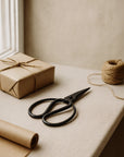 Forged Iron Scissors with handcrafted design styled on a neutral surface beside a wrapped gift, brown paper, and twine in a natural light setting