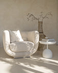 A serene living space featuring the KULALA Living curved bouclé chair in a soft ivory tone. Styled with a textured cushion, sculptural side table, and an earthy vase for a relaxed, modern aesthetic