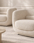 Francisco one seater armchairs in cream boucle with soft curved backs, styled in a refined neutral living room with a round marble coffee table and warm brass lamp accents.
