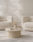 Francisco one seater armchairs in cream boucle with soft curved backs, styled in a refined neutral living room with a round marble coffee table and warm brass lamp accents.