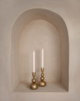 A pair of gold sculptural candlesticks with a polished brass finish styled in an arched wall niche