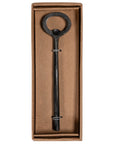 A handcrafted black iron bottle opener with a rustic finish, presented in a minimalist brown cardboard box