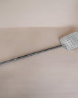A handcrafted metal spatula from KULALA Living, featuring a perforated stainless steel paddle and a long black iron handle for effortless pizza baking and serving
