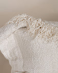 A natural-toned lumbar cushion with a woven texture, featuring delicate fringed edges, set against a neutral backdrop