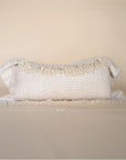 A natural-toned lumbar cushion with a woven texture, featuring delicate fringed edges, set against a neutral backdrop
