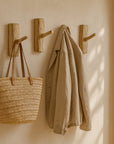 Set of KULALA Living Intonga Wall Hooks hand-carved from teak, styled in a warm mudroom setting with a hanging woven basket and linen coat.