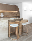 Close-up of a marble kitchen island styled with curved rattan barstools featuring white cushions, paired with soft lighting and earthy decor for a natural, relaxed look.