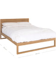 A sleek modern bed frame crafted from natural oak, featuring a minimalist open-base design. The bed is styled with crisp white linen and plush pillows, offering a refined and contemporary bedroom aesthetic