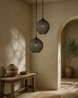 Kulo Pendant Light in black, handwoven and suspended in an arched hallway with organic textures and natural timber bench.