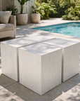 White Kuzu stool set arranged as a sculptural cluster beside a sunlit pool, featuring solid timber blocks with visible grain and soft coastal styling.