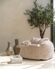 The Kulala Living luxe boucle bean bag in a serene, sunlit setting, styled with earthy-toned decor and an olive tree. Featuring a soft natural texture, this oversized bean bag blends modern comfort with relaxed elegance, perfect for a tranquil living space
