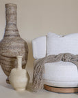A cozy interior setting featuring a boucle swivel lounge chair with a wooden base, accompanied by textured decorative vases and a soft woven throw in neutral tones.